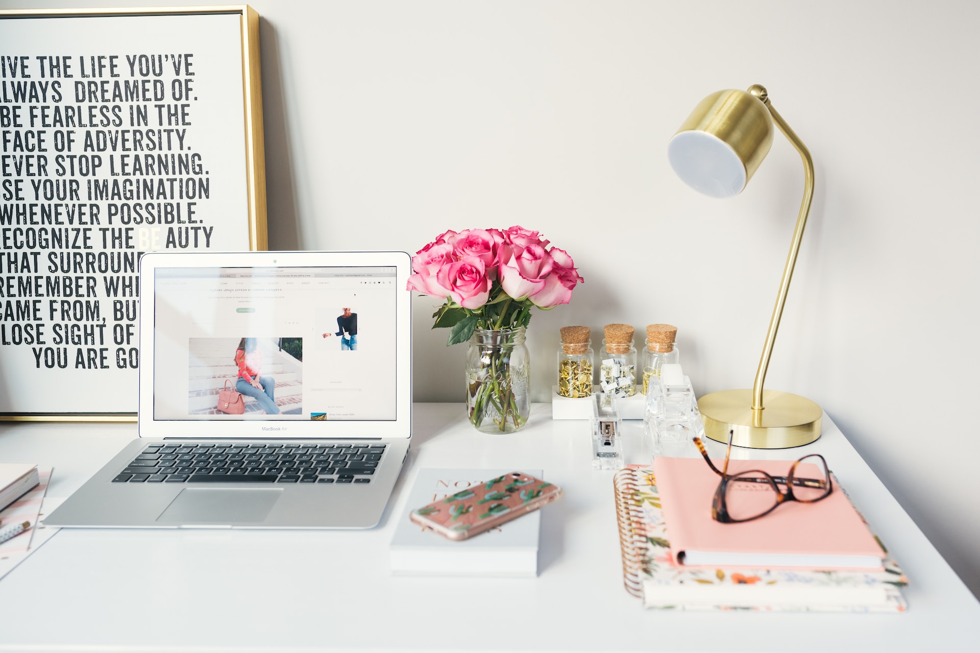 Laptop with motivational poster, flowers, lamp and office supplies